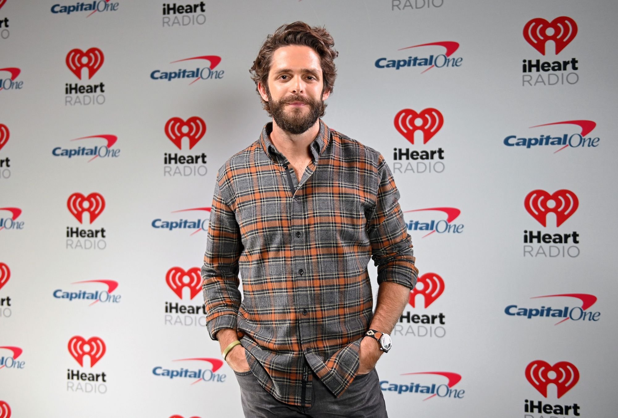 Thomas Rhett smiling in front of a white background with repeating logos