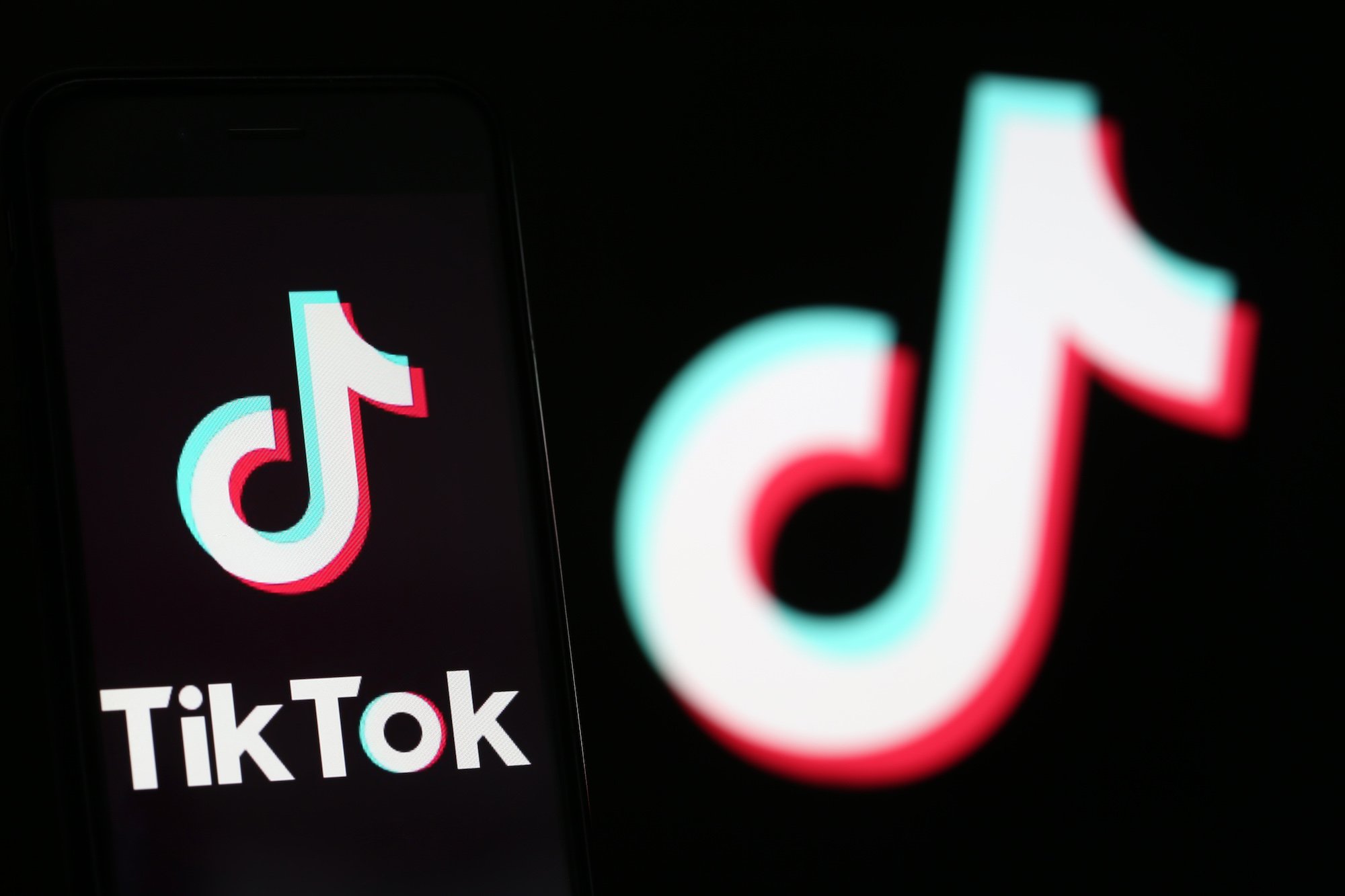 Illustration of the logo for TikTok displayed on the screen of a smartphone in front of a TV screen displaying the TikTok logo