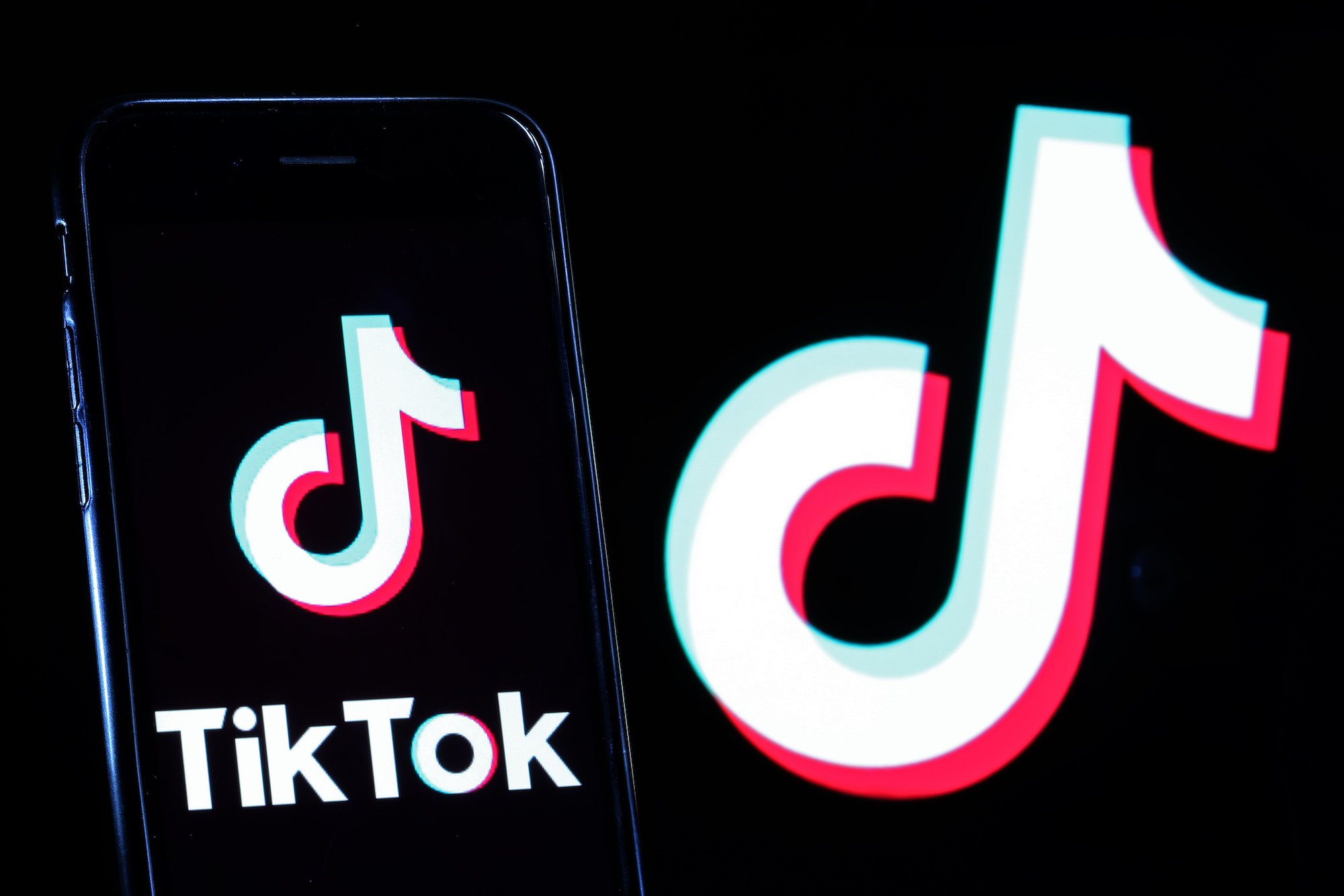 TikTok logo displayed on a smartphone in front of a screen with the TikTok logo