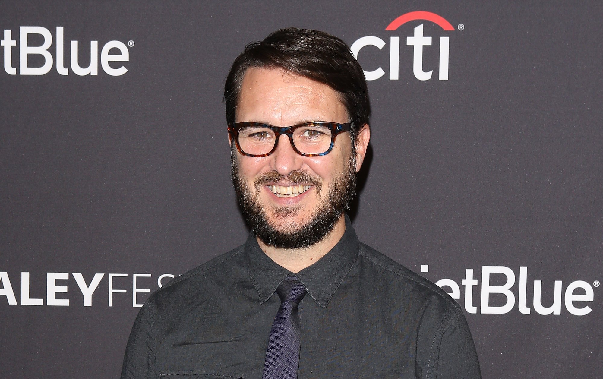 Wil Wheaton smiling in front of a dark blue background