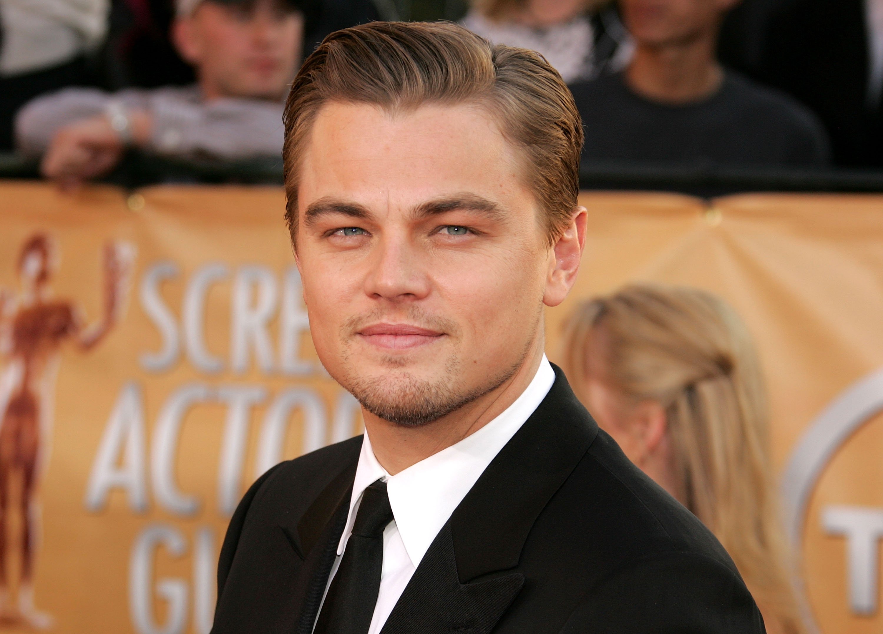 Leonardo DiCaprio wearing a suit and tie and standing in front of a poster