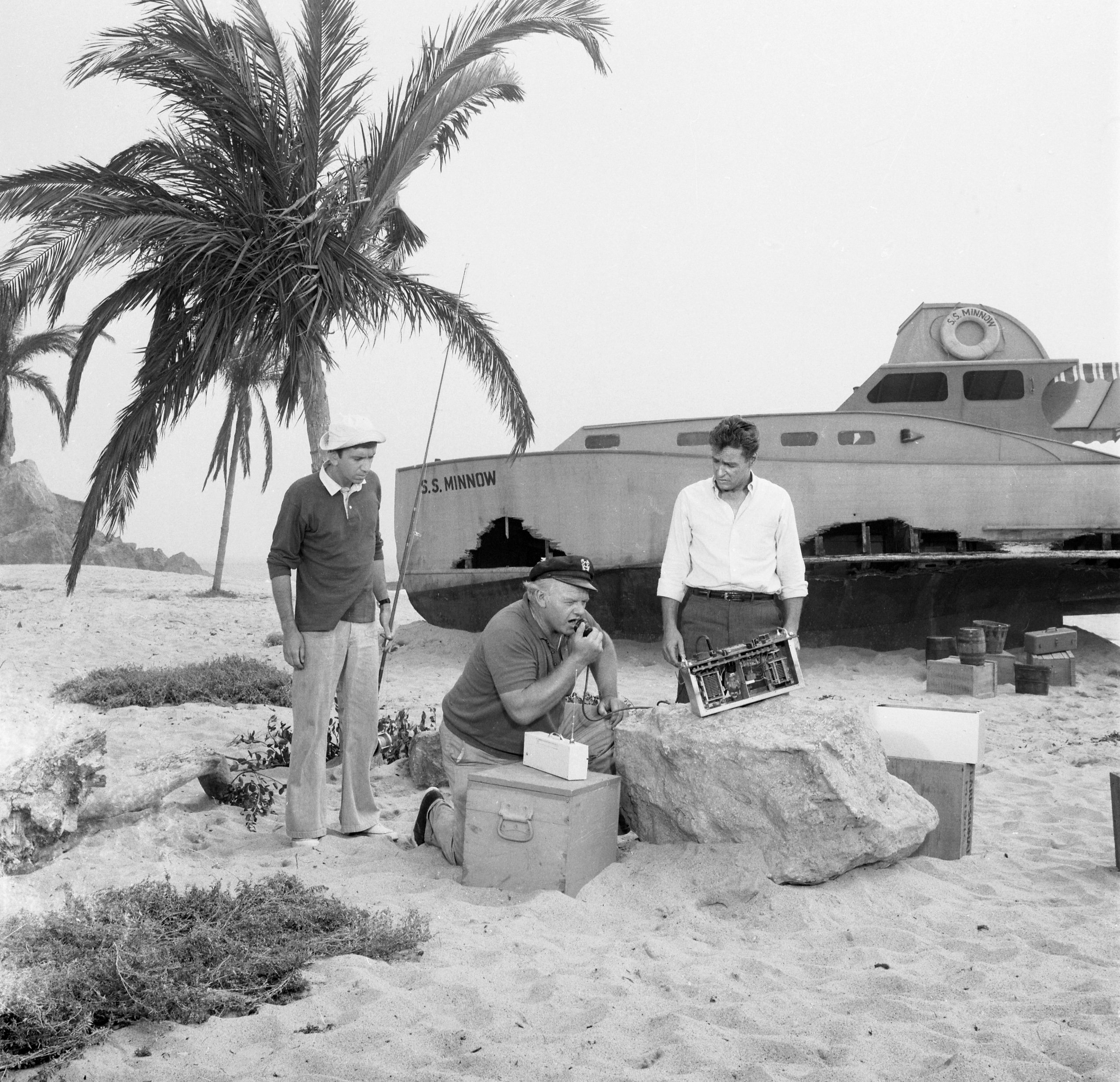 Gilligan, the Skipper, and the Professor near palm trees