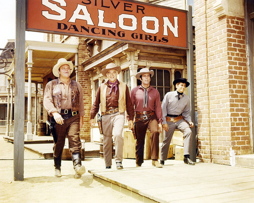 (L-R) Dan Blocker as Eric 'Hoss' Cartwright, Lorne Greene as Ben Cartwright, Pernell Roberts as Adam Cartwright and Michael Landon as Joseph 'Little Joe' Cartwright smiling, walking under a saloon sign