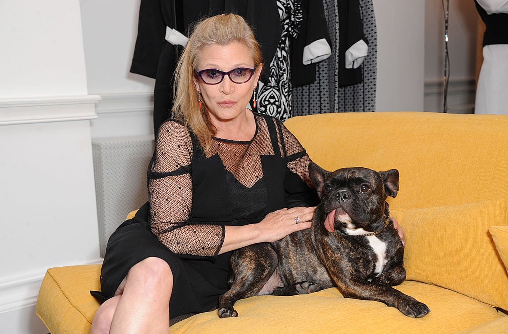 Carrie Fisher smiling, sitting with her dog on a yellow couch