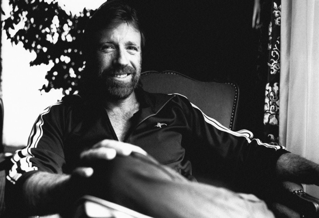 Chuck Norris smiling at the camera, in black and white
