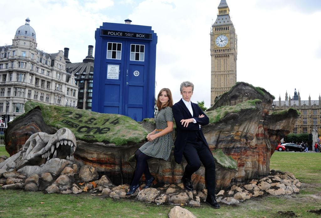 (L-R) Jenna Coleman and Peter Capaldi leaning against a rock, in front of a TARDIS