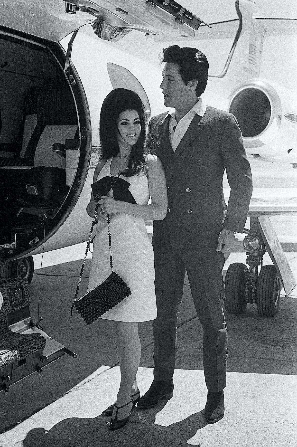 Elvis Presley and his bride, Priscilla Ann Beaulieu smile happily as they prepare to board a chartered jet airplane