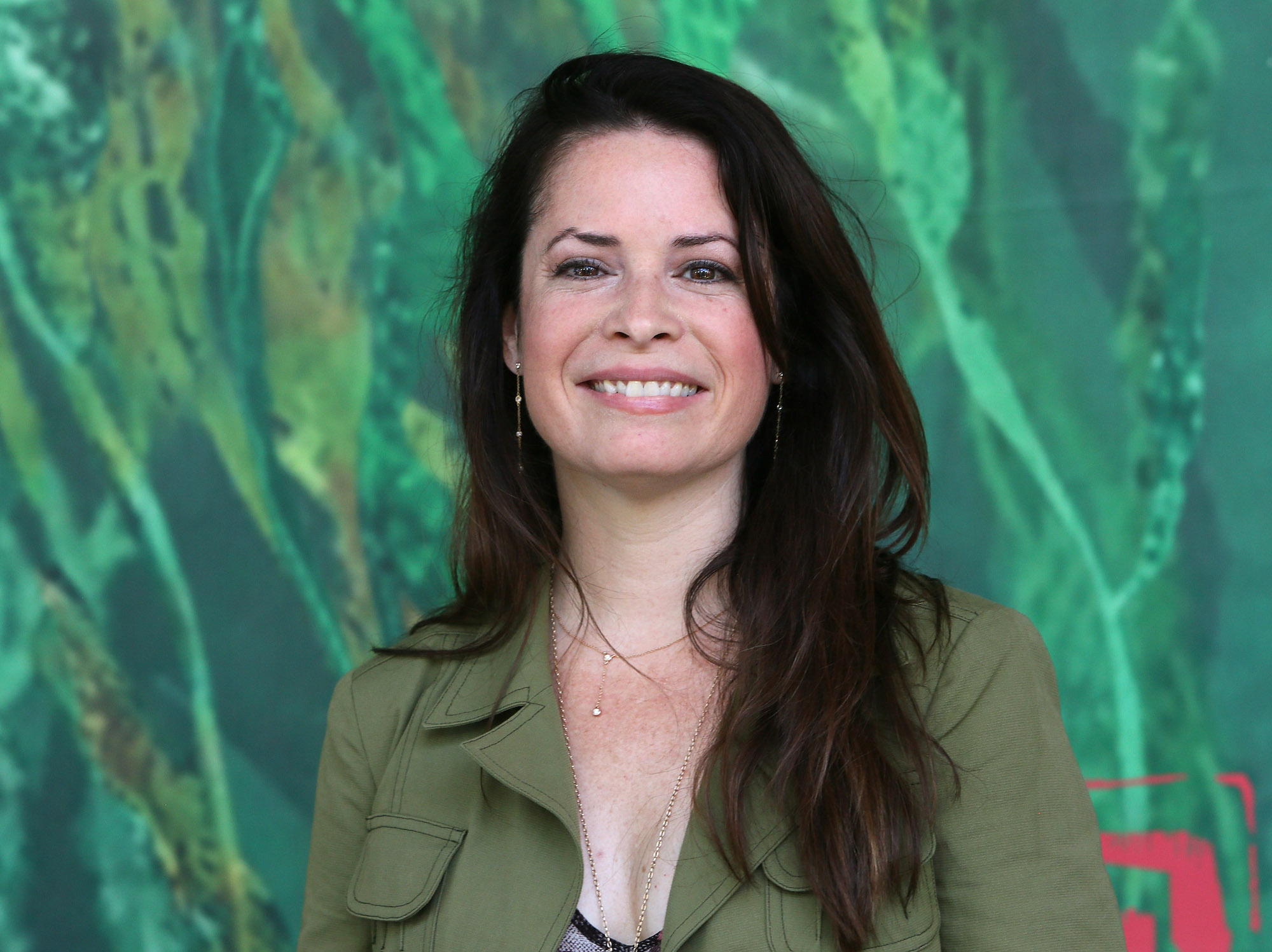 Holly Marie Combs smiling in front of a green background