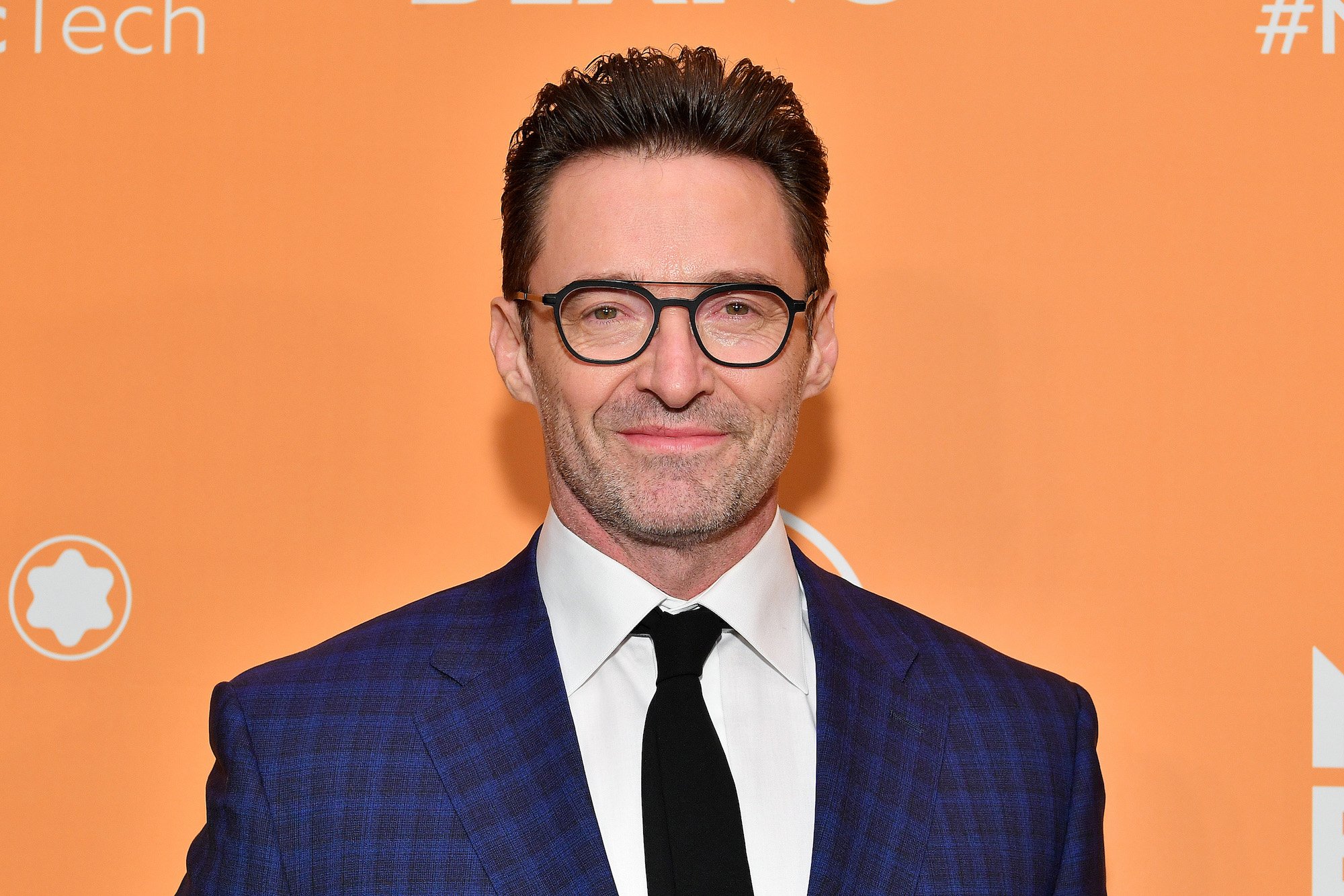 Hugh Jackman smiling in front of an orange background