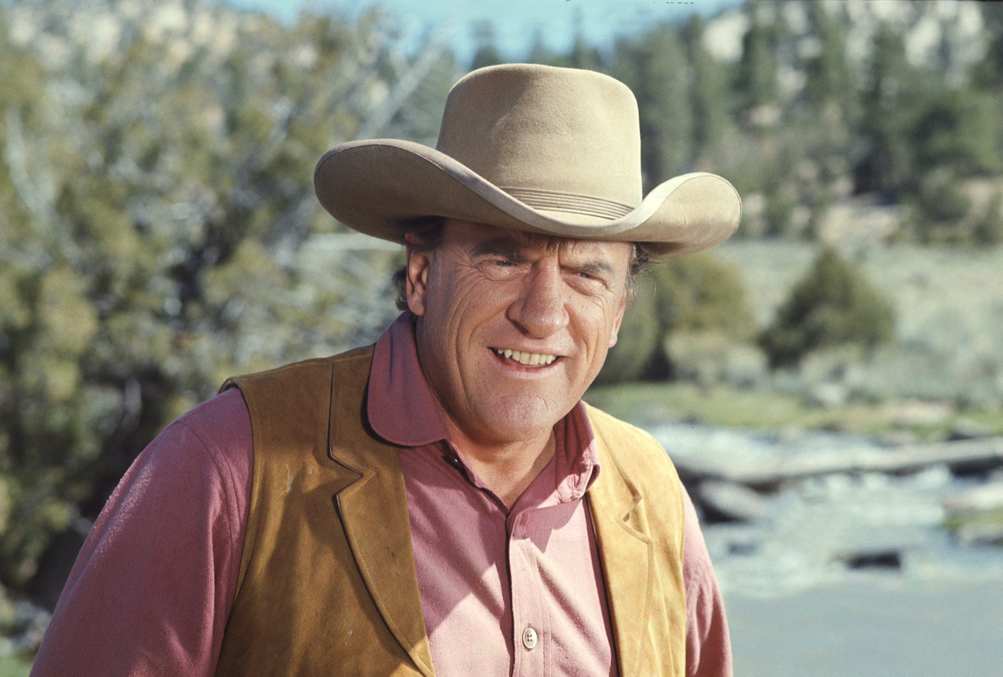 James Arness as Marshal Matt Dillon smiling in front of a blurred background, dressed in western gear