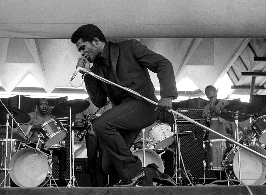 James Brown singing into a microphone, bending down
