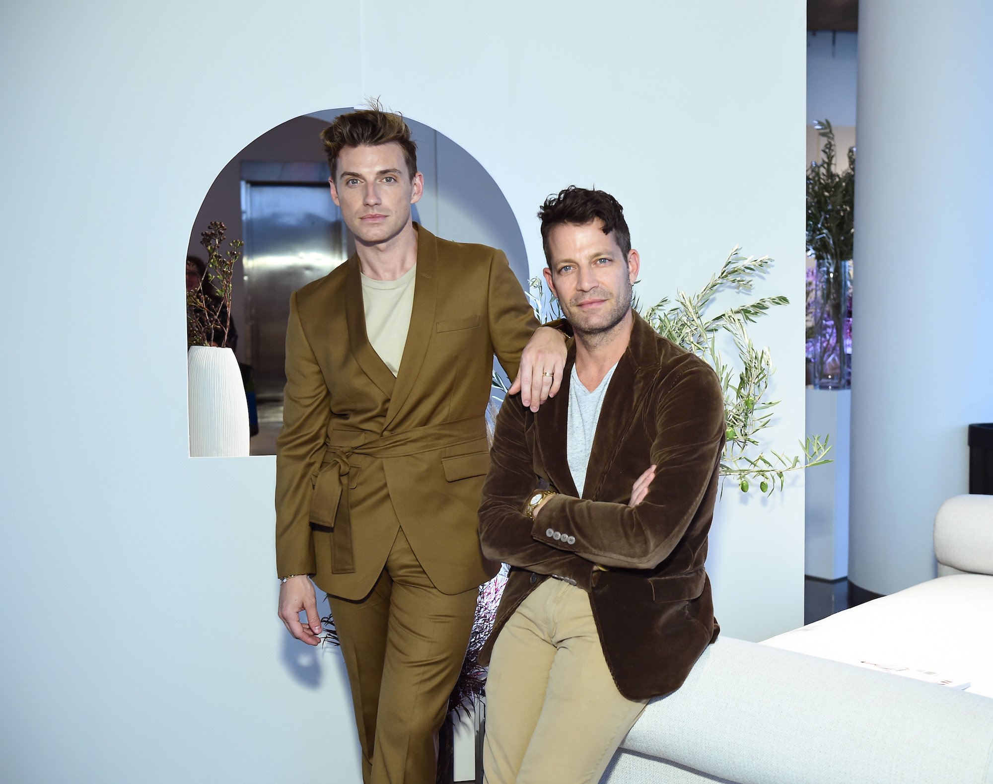 (L-R) Jeremiah Brent and Nate Berkus slightly smiling in a white room, leaning on a white couch