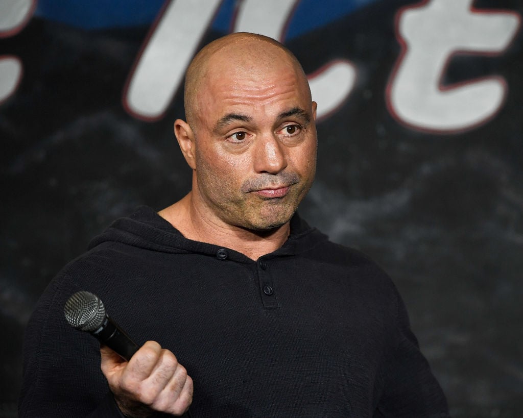 Joe Rogan shrugging, holding a microphone