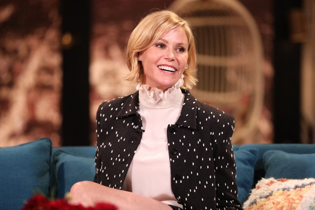 Julie Bowen smiling, sitting on a couch, in front of a blurred background