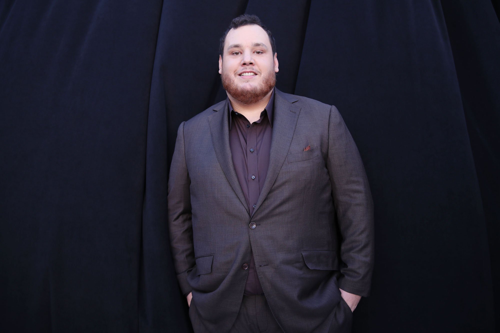 Luke Combs smiling in front of a black background