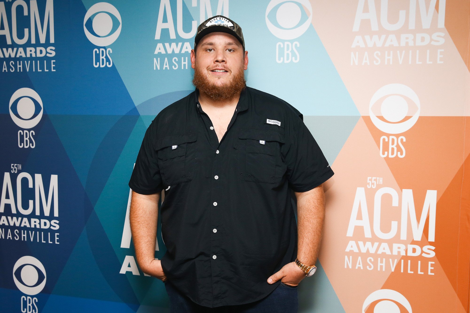 Luke Combs smiling slightly in front of a blue and orange background