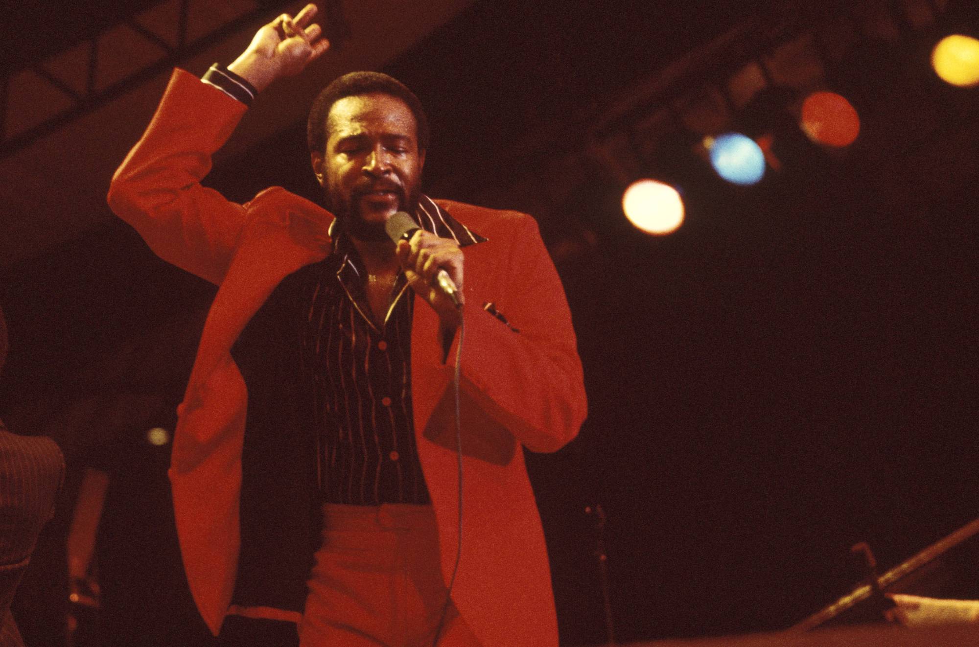 Marvin Gaye on stage, singing into a microphone, wearing a red outfit