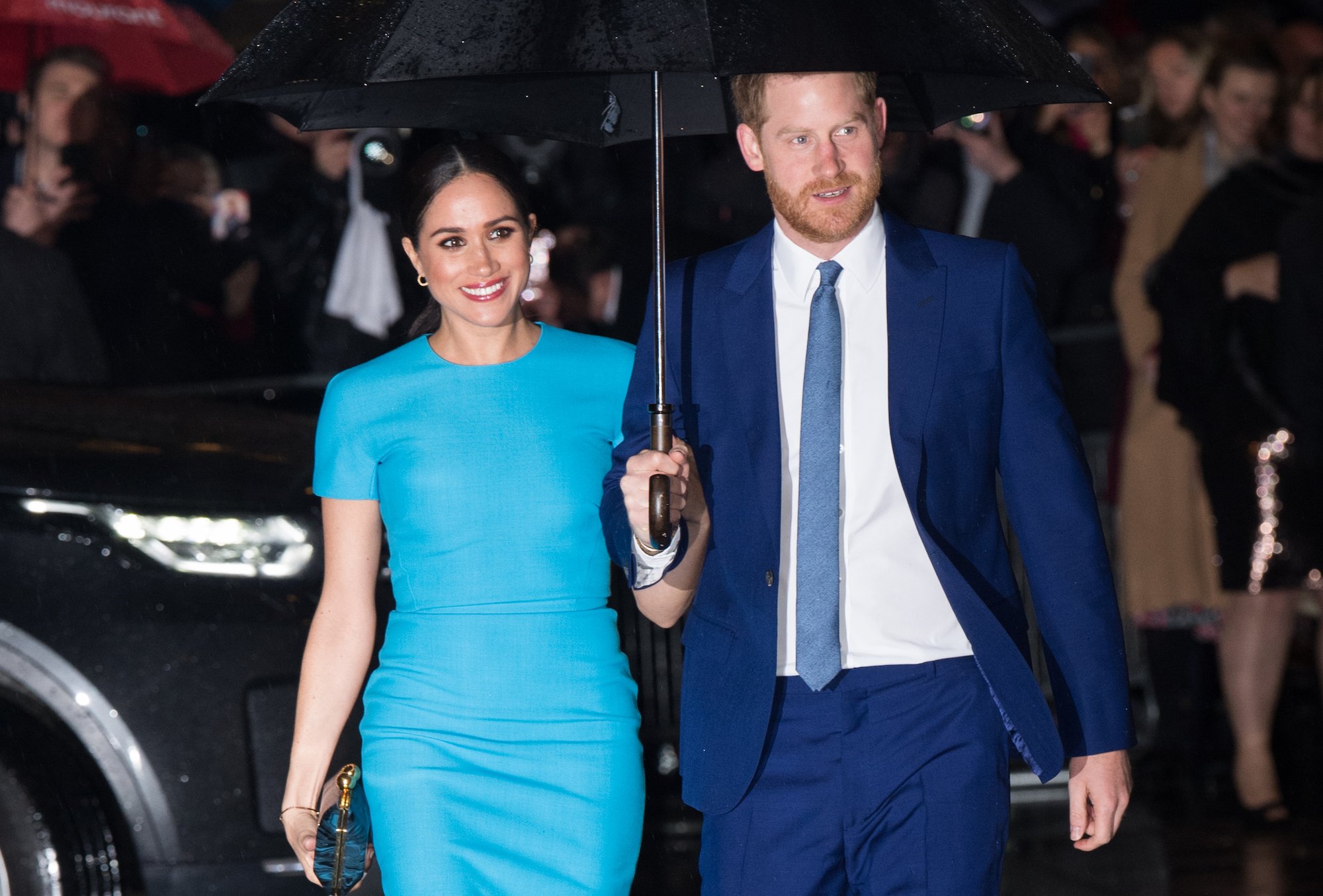 Meghan Markle and Prince Harry smiling, walking under and umbrella