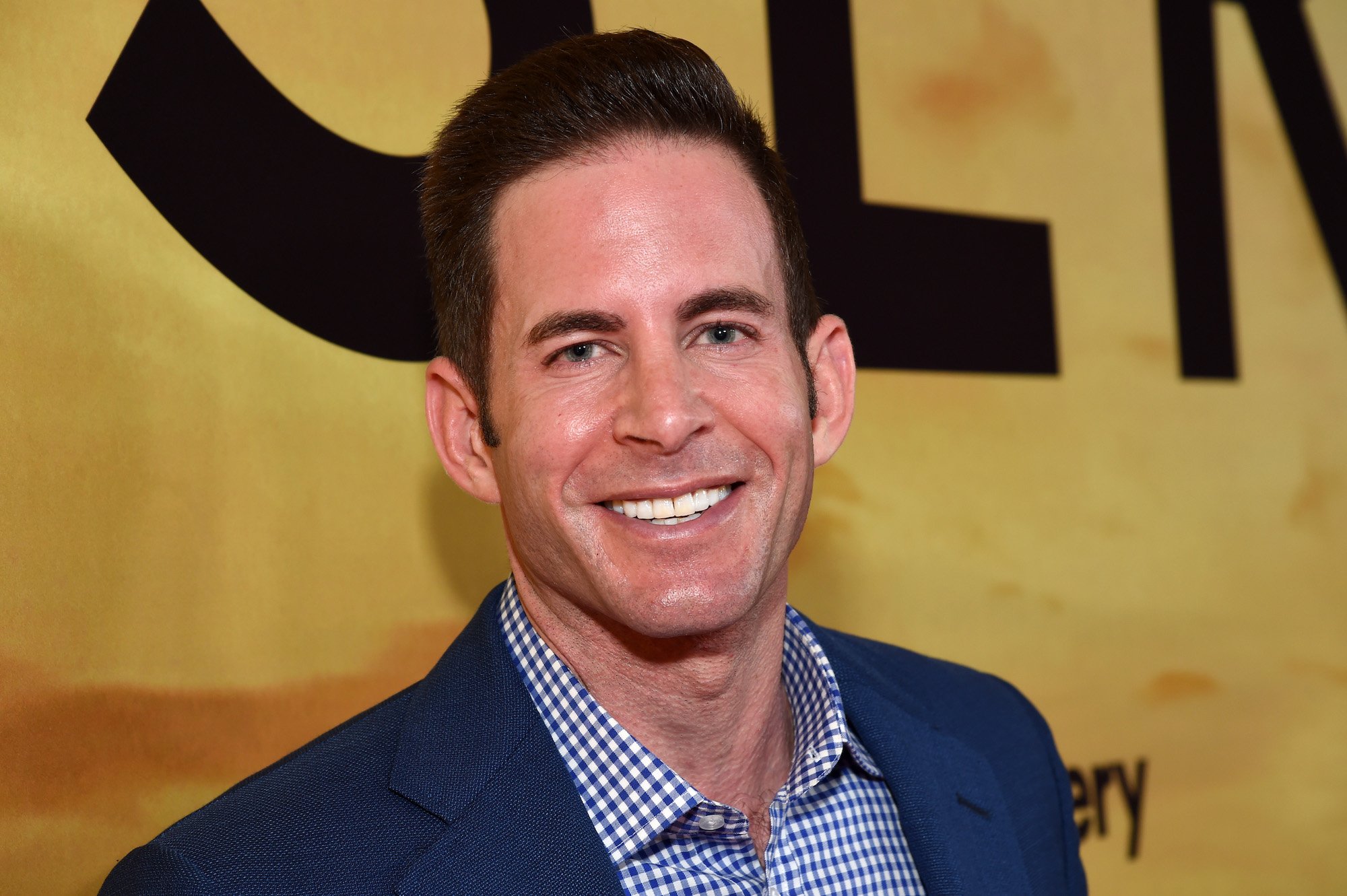 Tarek El Moussa smiling in front of a yellow background