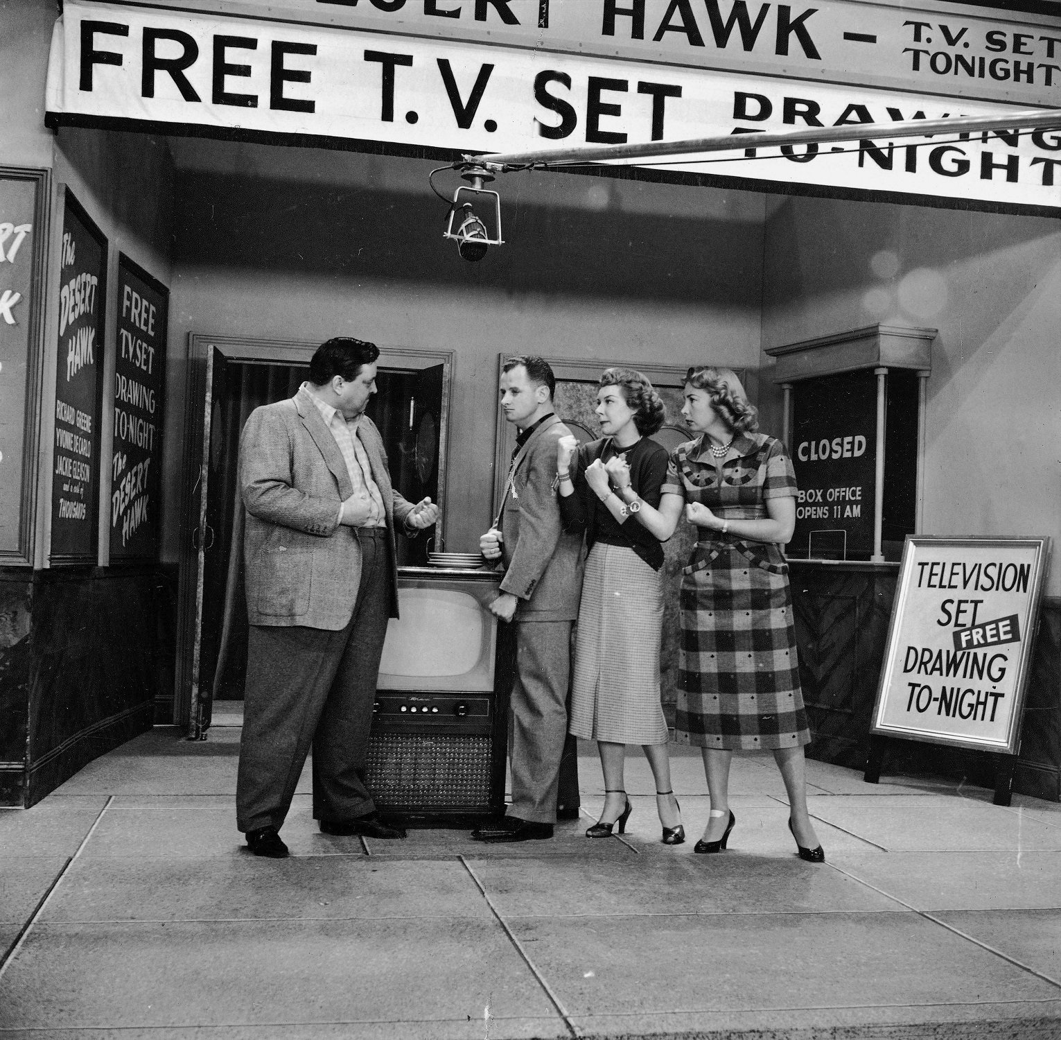 Jackie Gleason, Art Carney, Joyce Randoph and Audrey Meadows stand by a banner announcing a raffle for a new TV on the set of 'The Honeymooners'
