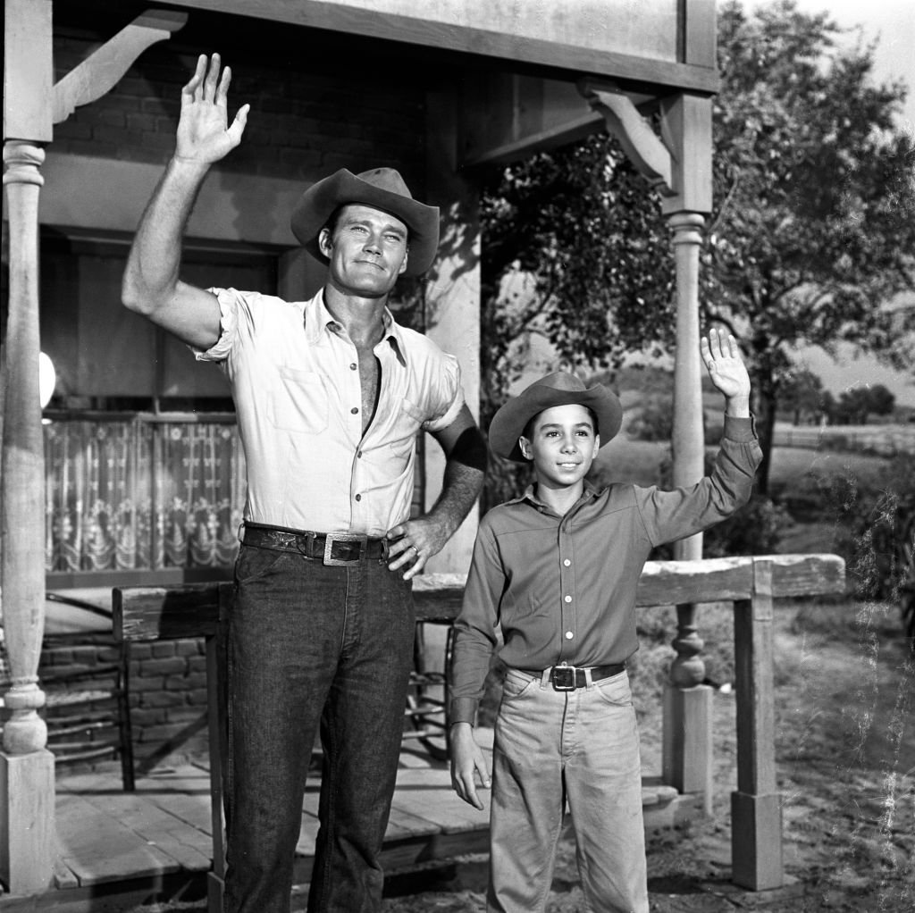 (L-R) Chuck Connors as Lucas McCain and Johnny Crawford as Mark McCain smiling and waving