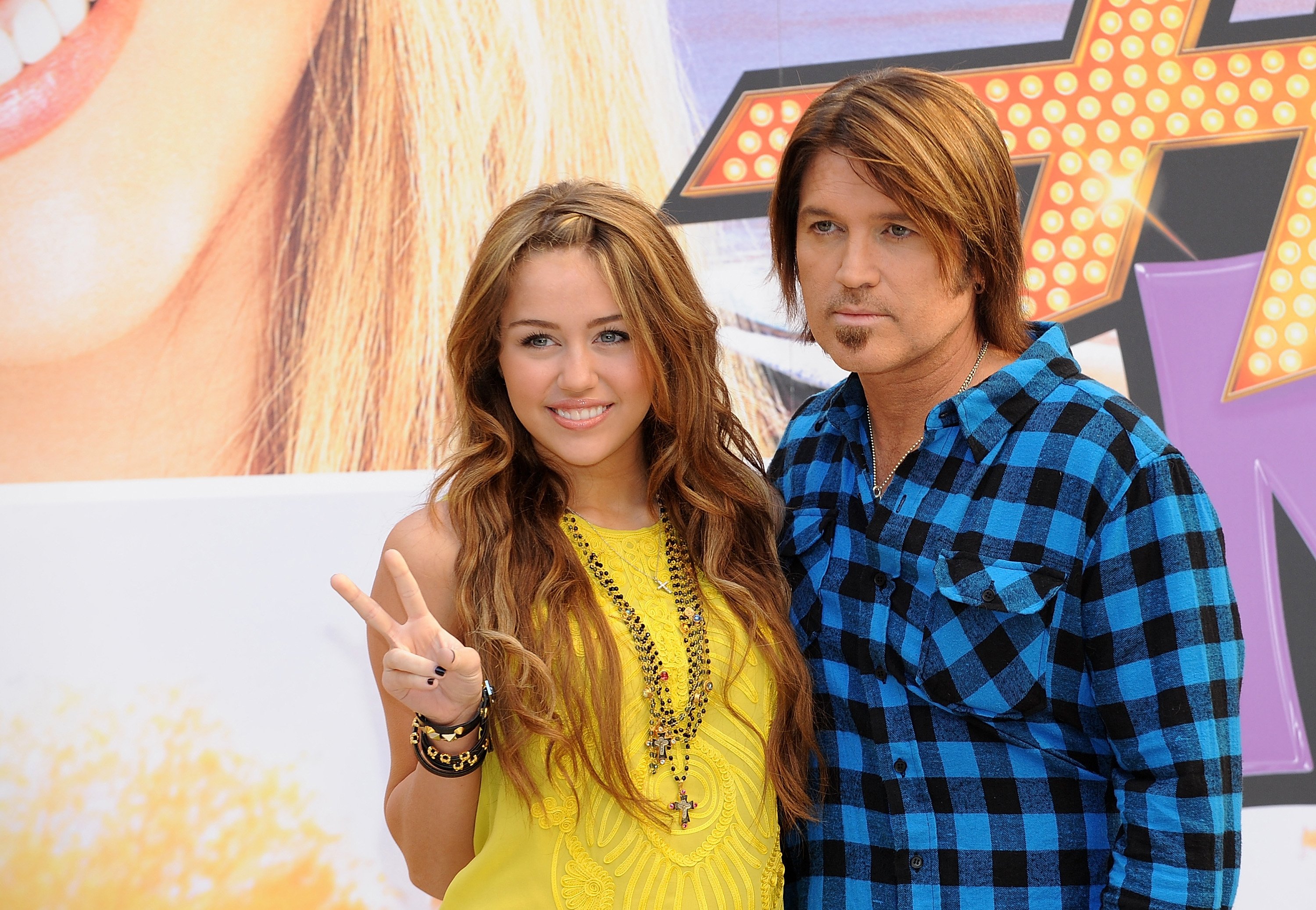 Miley Cyrus and Billy Ray Cyrus in front of a Hannah Montana poster