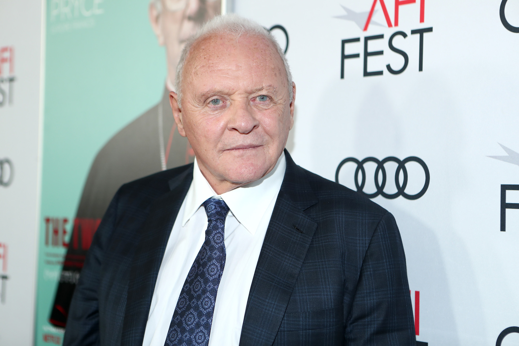 Anthony Hopkins standing in front of a white background with logos