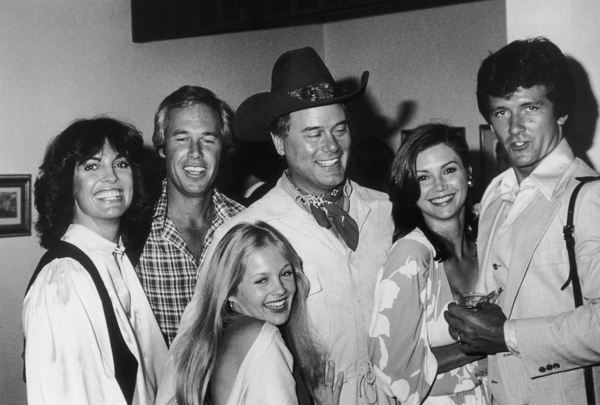 (L-R) Linda Gray, Steve Kanaly, Charlene Tilton, Larry Hagman, Victoria Principal and Patrick Duffy smiling, in black and white