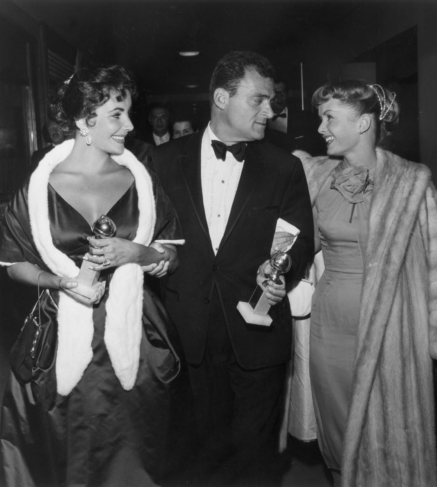 From left to right, British-born actor Elizabeth Taylor and her husband, film producer Mike Todd (1909 - 1958), hold their Golden Globe awards while walking with American actor Debbie Reynolds at the Hollywood Foreign Press Association Awards Dinner in Los Angeles. Taylor won a special award for consistent performance, and Todd produced Michael Anderson's 1957 film, 'Around the World in Eighty Days,' which received the Best Motion Picture- Drama award. 