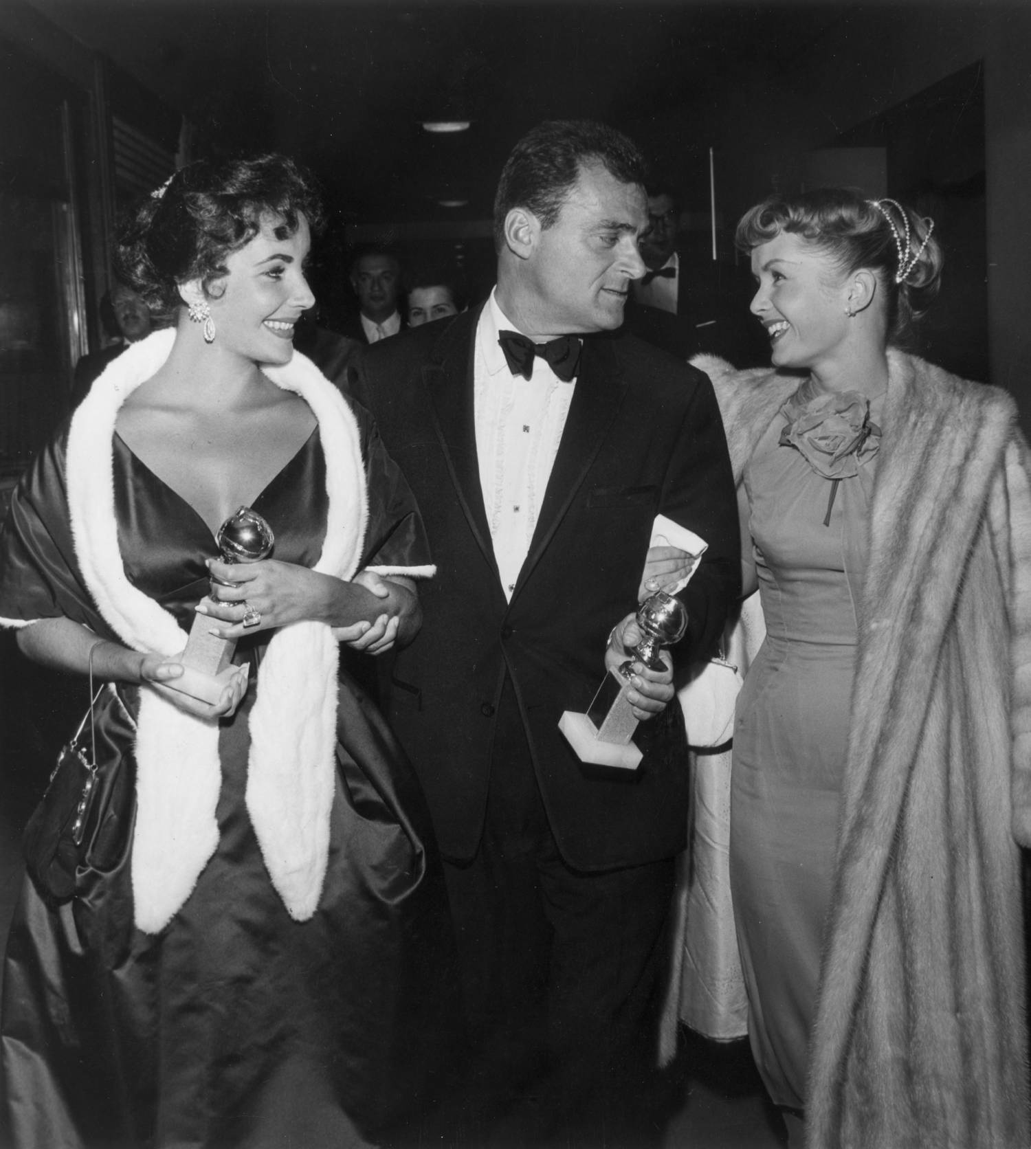 From left to right, British-born actor Elizabeth Taylor and her husband, film producer Mike Todd (1909 - 1958), hold their Golden Globe awards while walking with American actor Debbie Reynolds at the Hollywood Foreign Press Association Awards Dinner in Los Angeles. Taylor won a special award for consistent performance, and Todd produced Michael Anderson's 1957 film, 'Around the World in Eighty Days,' which received the Best Motion Picture- Drama award.