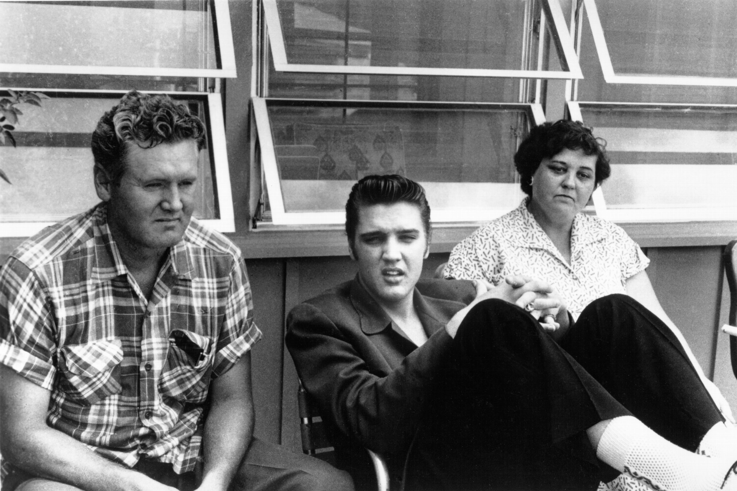 Elvis Presley sitting with his parents Vernon and Gladys in 1956 in a black-and-white image