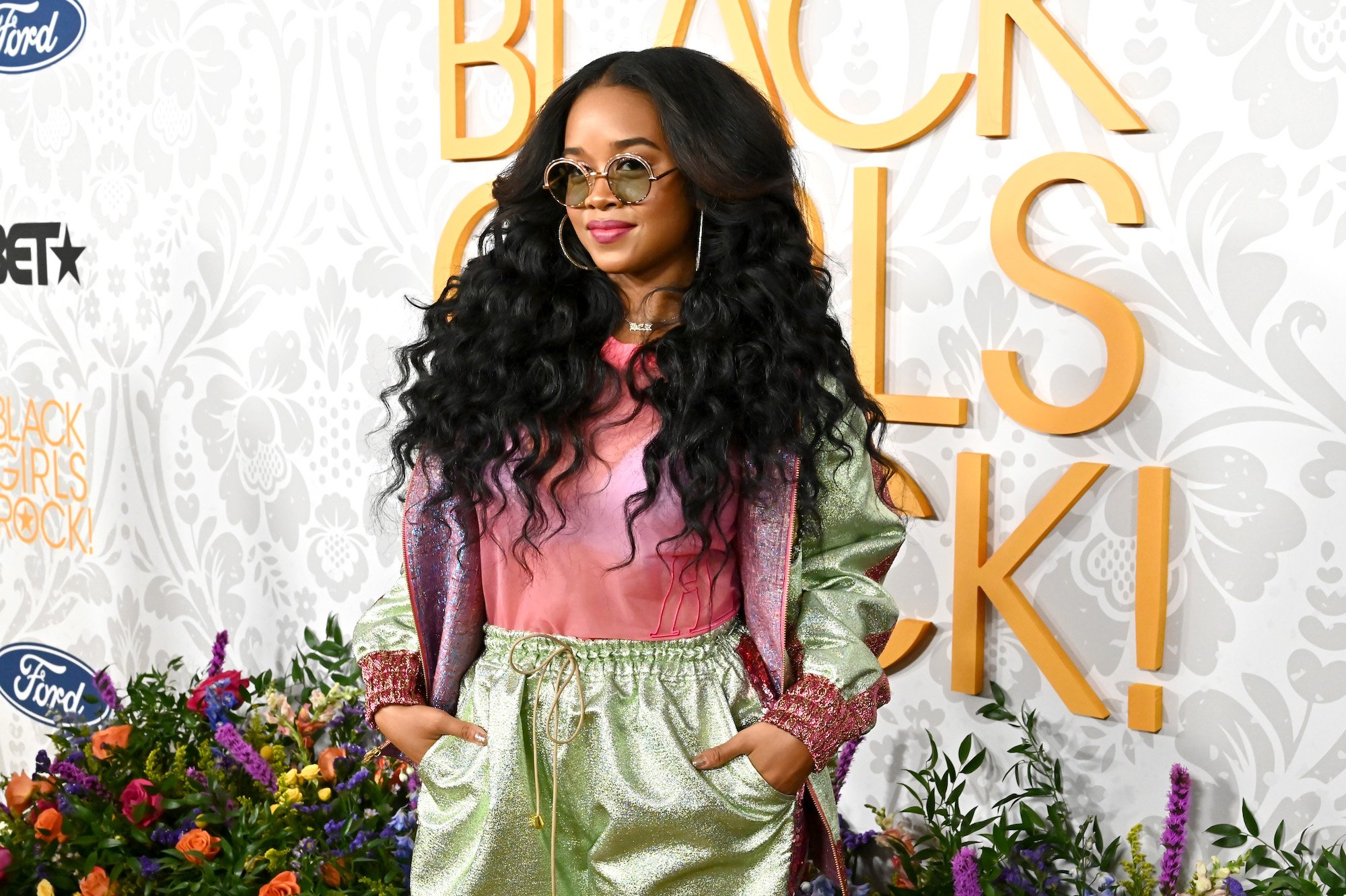 H.E.R. smiling in front of a textured background, looking to the left