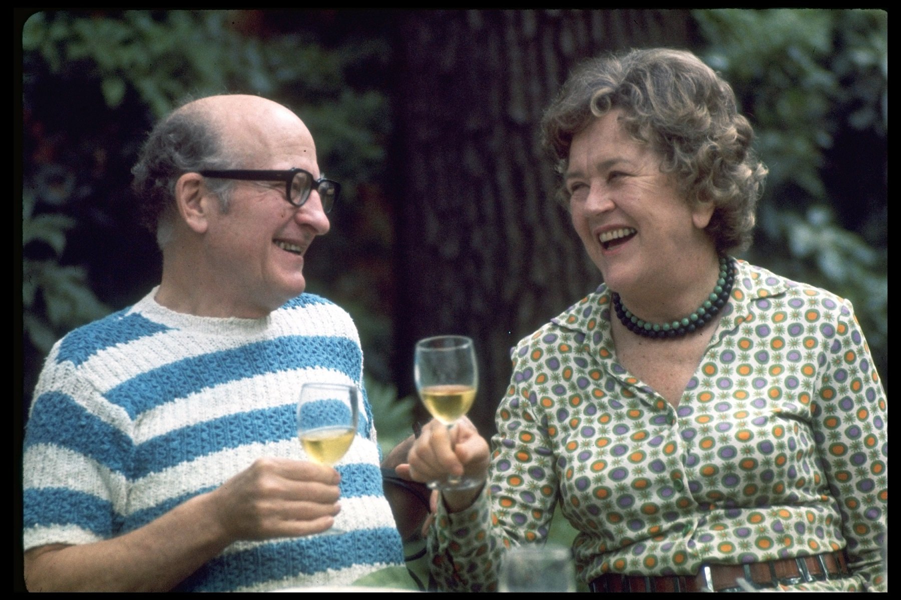 Julia Child (L) and husband, Paul Child, enjoying a glass of wine in outdoor setting.