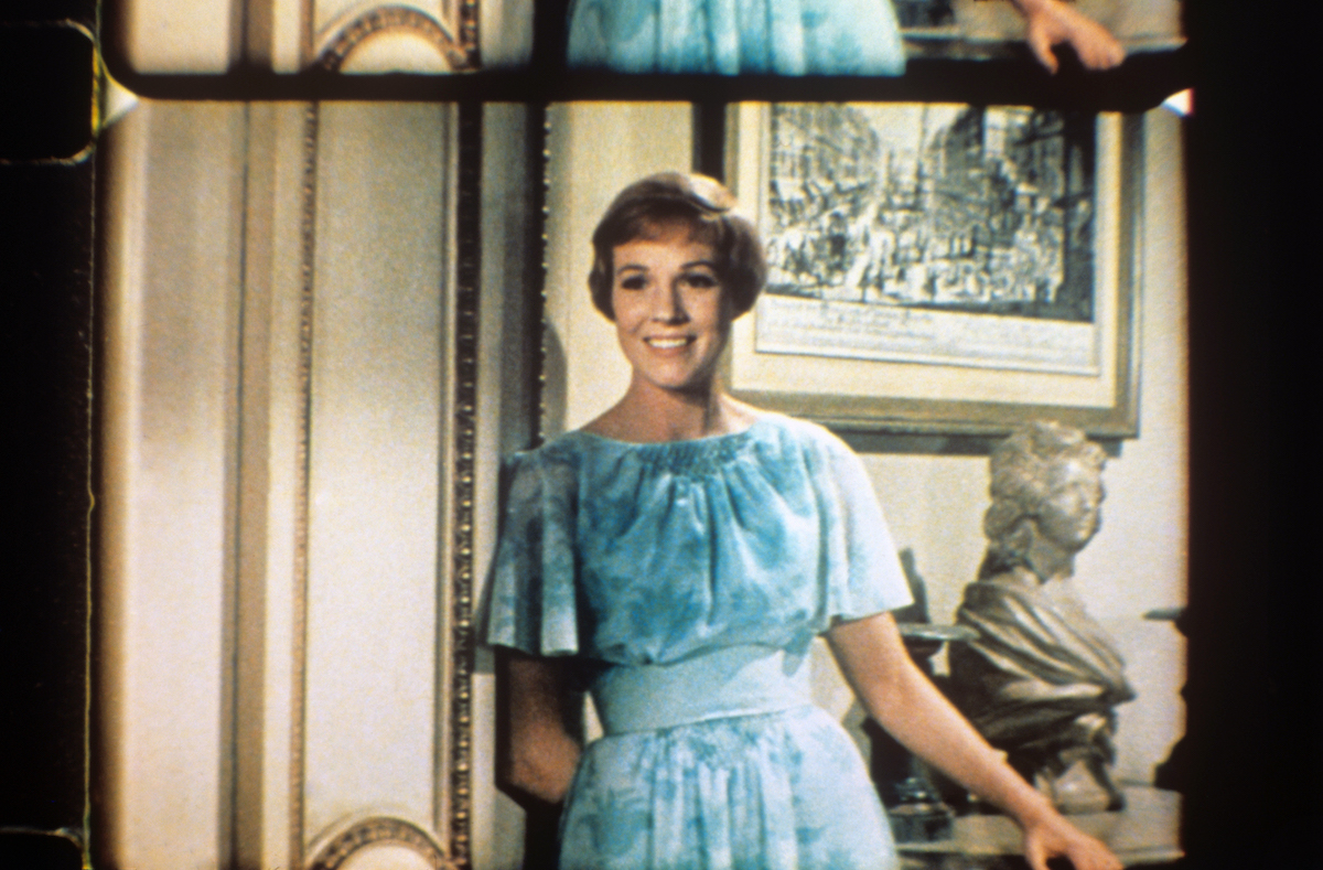 The British actress Julie Andrews, the pseudonym of Julia Elizabeth Wells, smiling in a blue dress, with a hand behind her back, in a scene of the film The Sound of Music by Robert Wise |  Mondadori via Getty Images