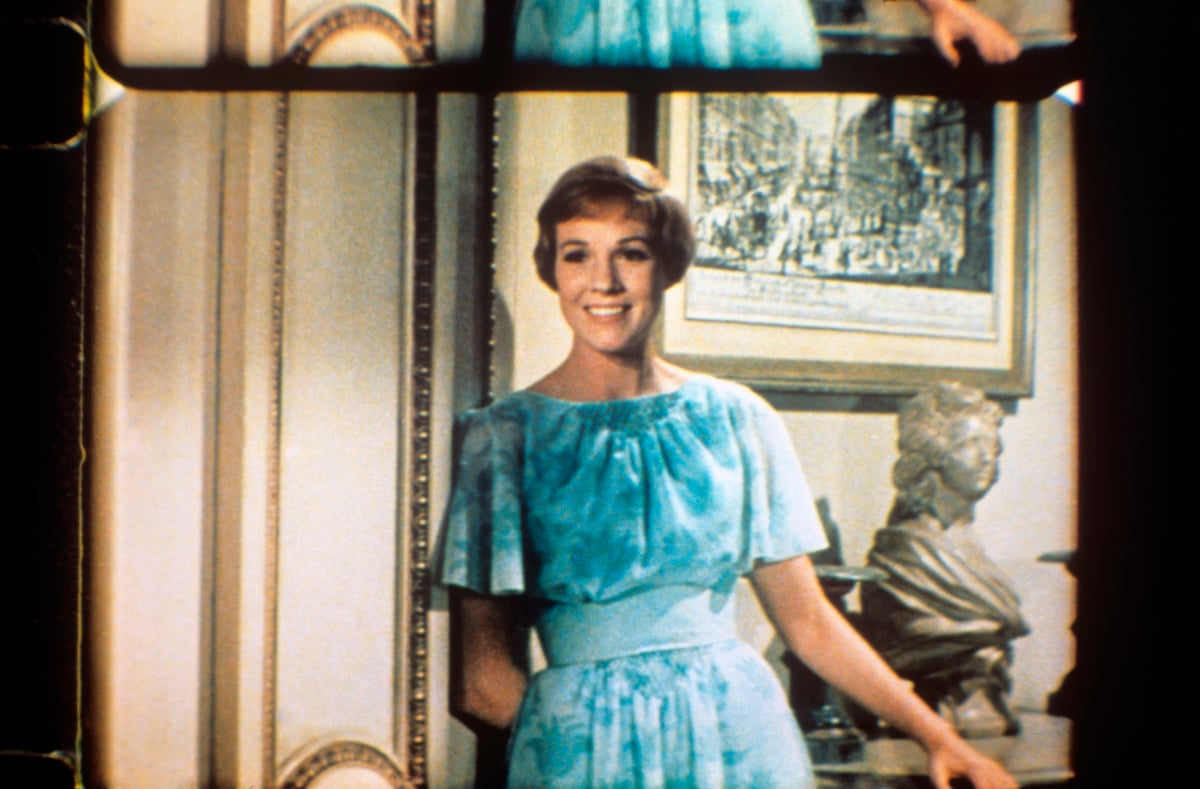 The British actress Julie Andrews, the pseudonym of Julia Elizabeth Wells, smiling in a blue dress, with a hand behind her back, in a scene of the film The Sound of Music by Robert Wise |  Mondadori via Getty Images