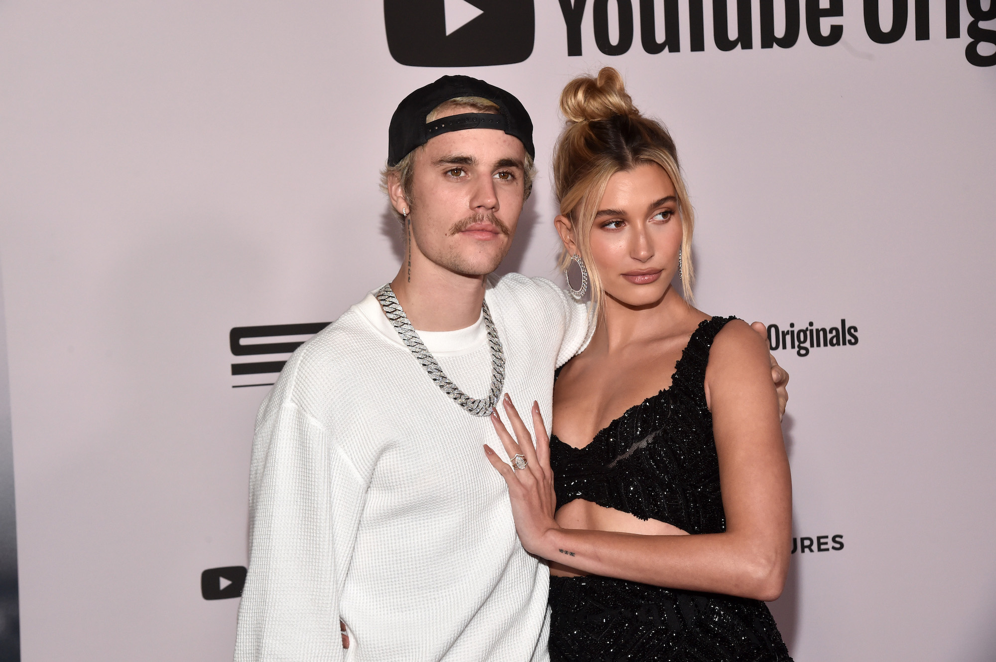(L-R) Justin Bieber and Hailey Bieber smiling in front of a pink background