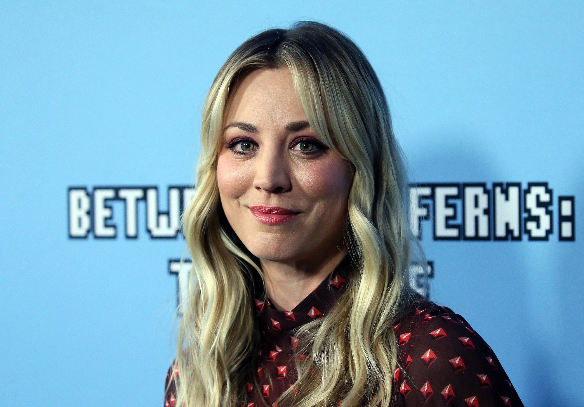 Kaley Cuoco smiling in front of a blue background