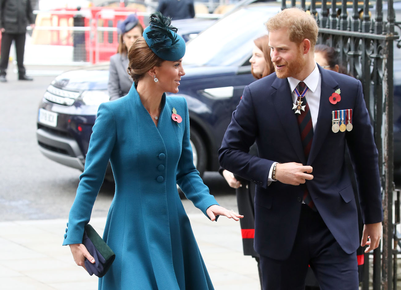 Kate Middleton wearing a teal jacket walking next to Prince Harry in a suit