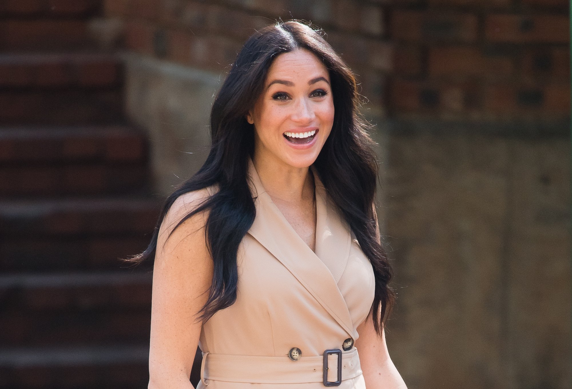 Meghan Markle smiling in front of a brick building