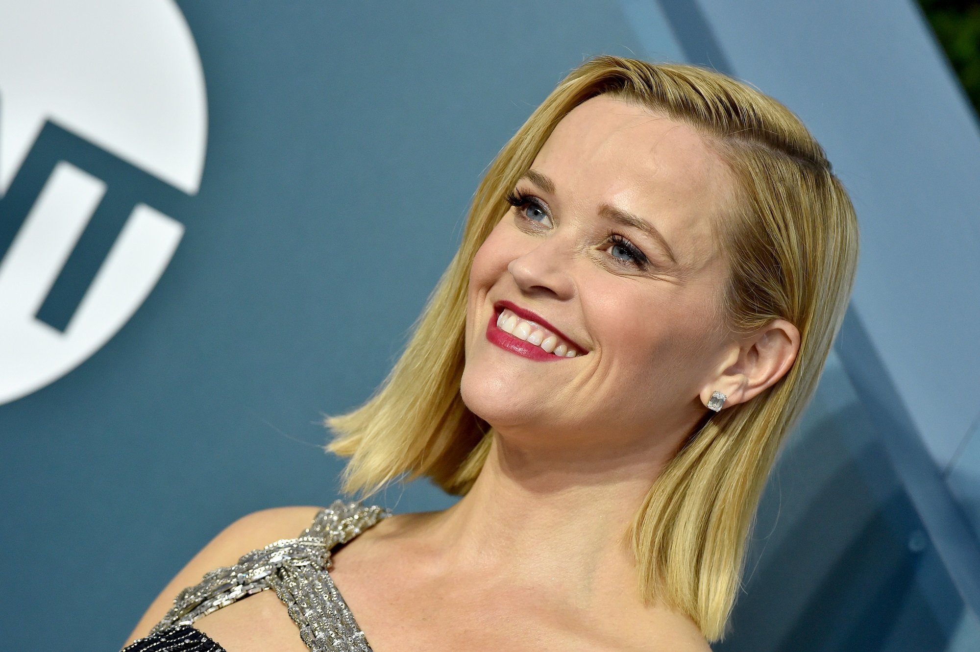 Reese Witherspoon smiling in front of blue/green background