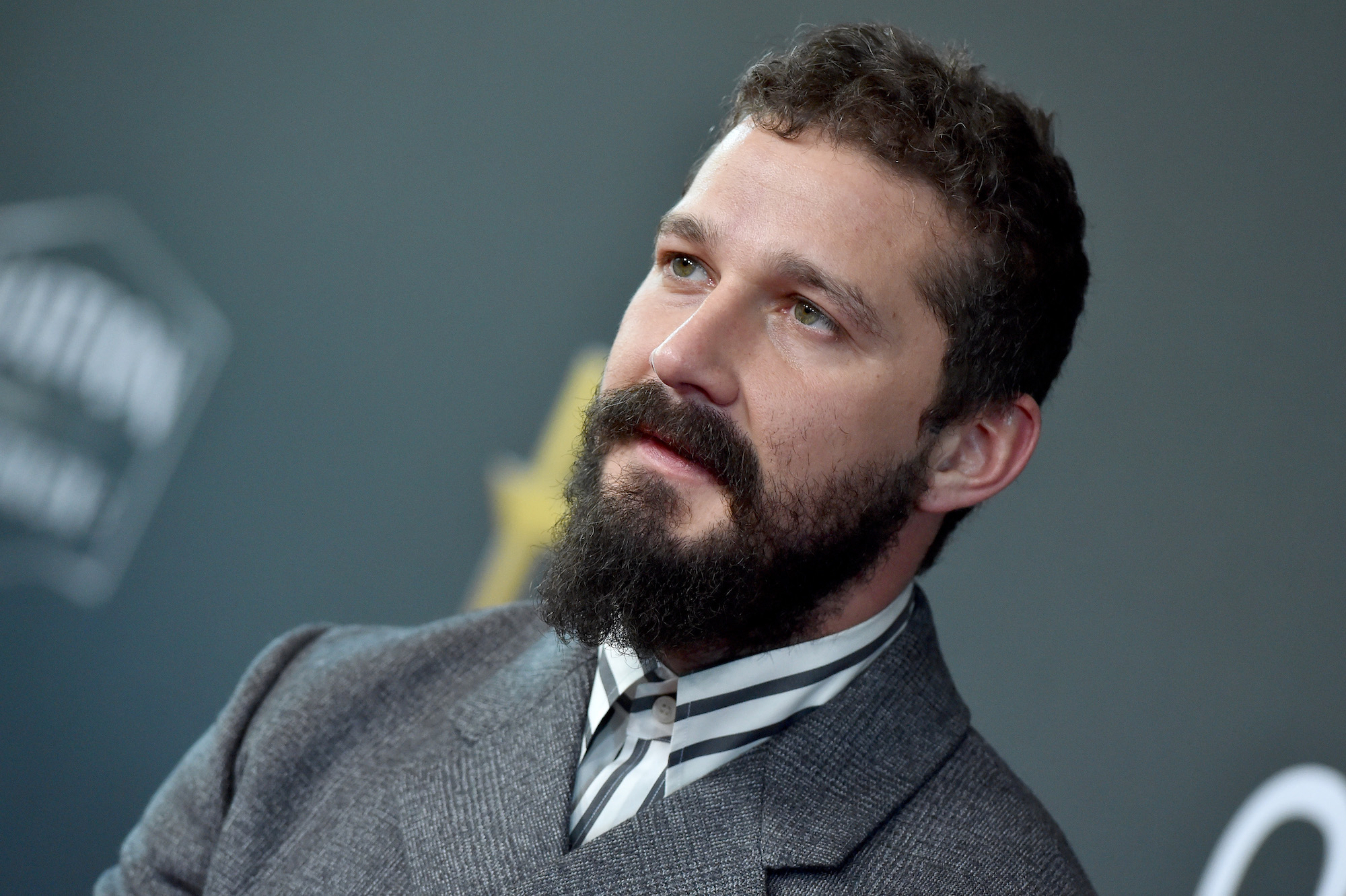 Shia LaBeouf looking off camera in front of a gray background