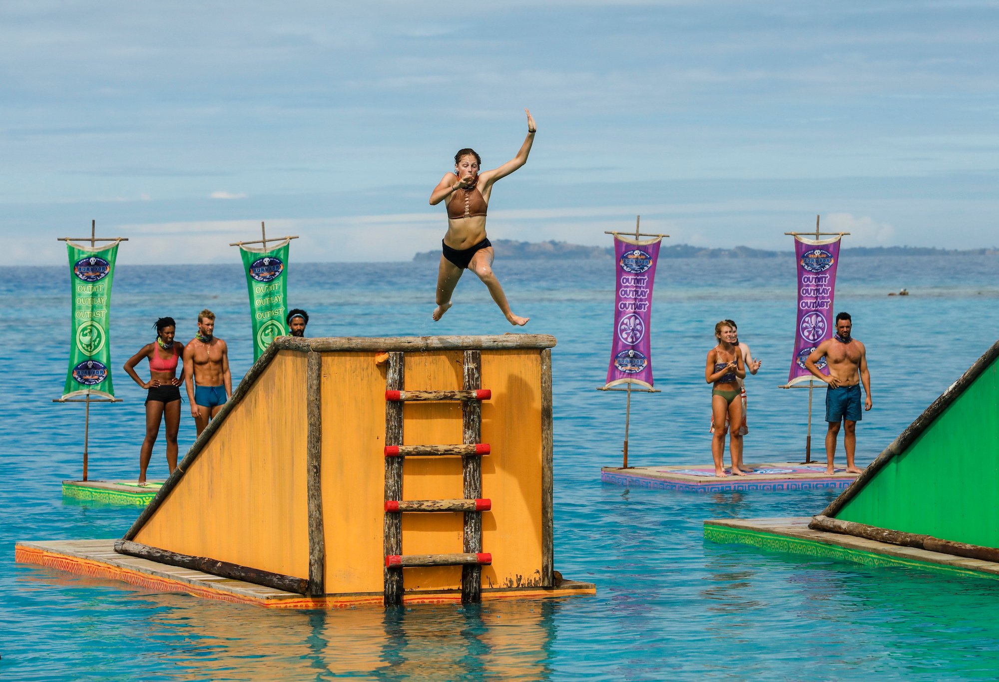 Survivor contestants competing on the show, in the water, with one contestant jumping off a platform
