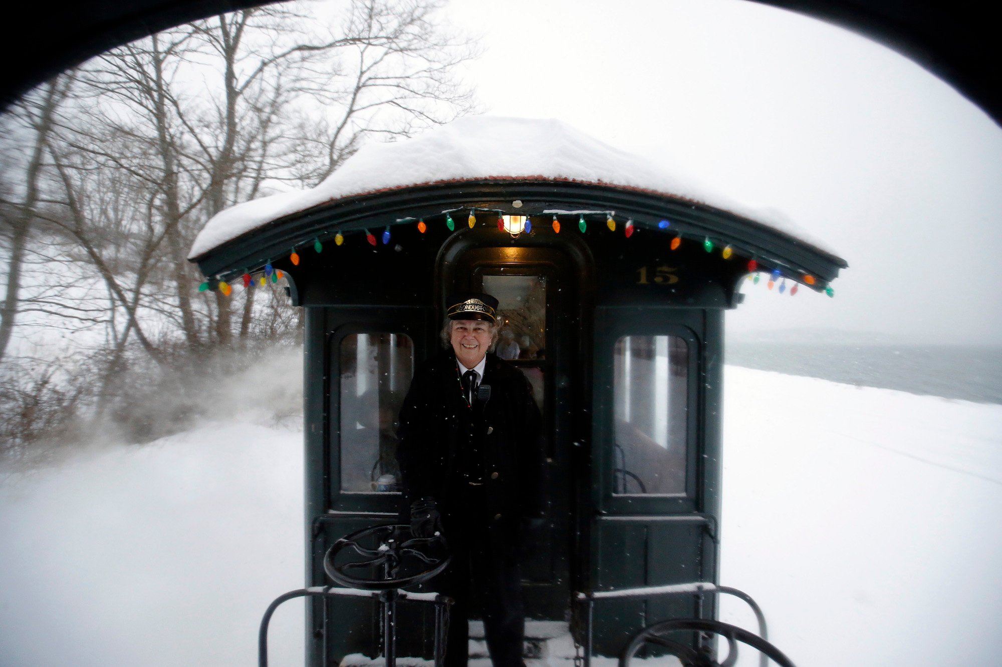 Conductor Sharon Roberts smiling on The Polar Express train, decorated with lights and covered in snow