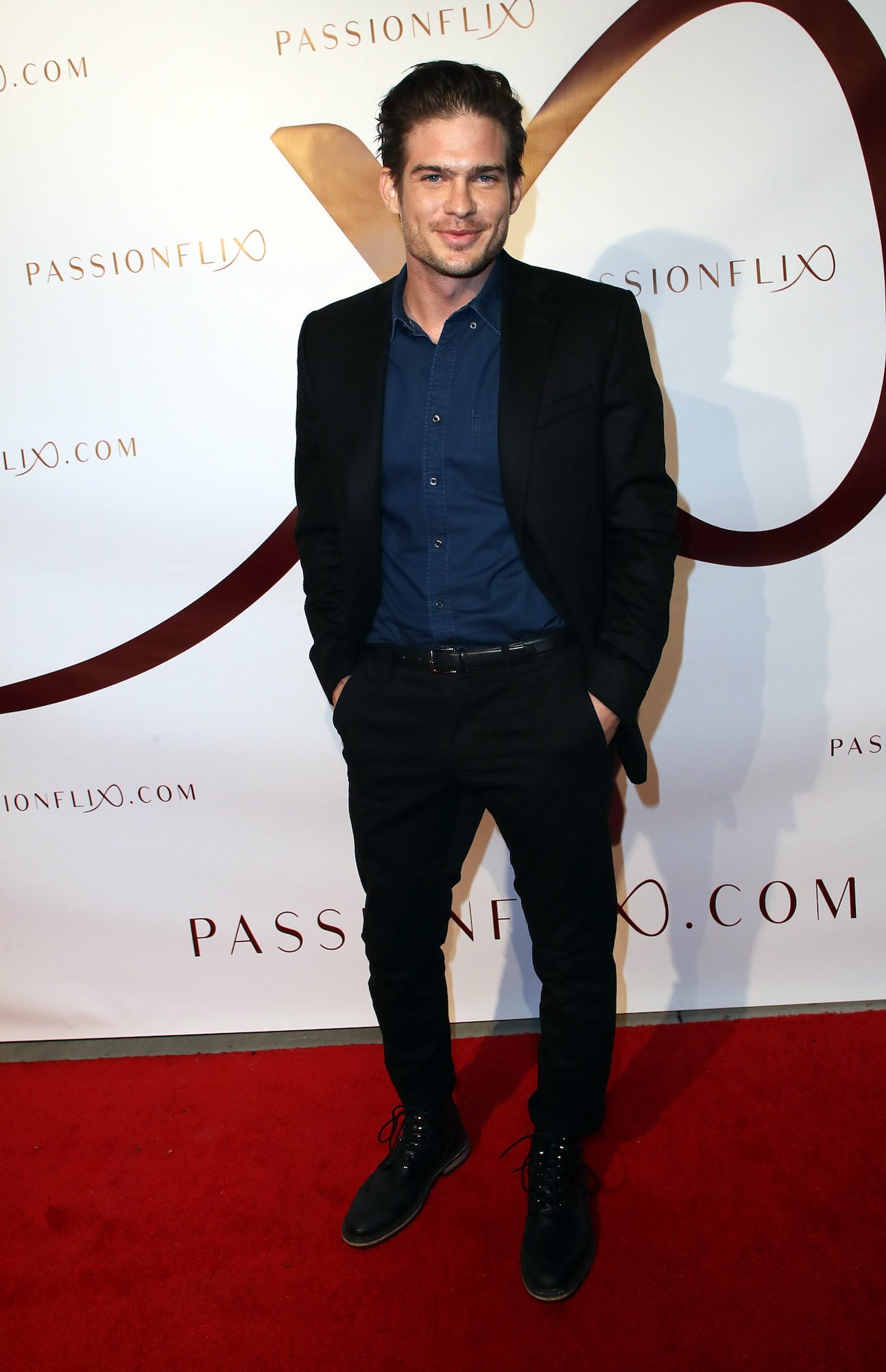 Tyler Johnson smiling in front of a white backdrop on a red carpet