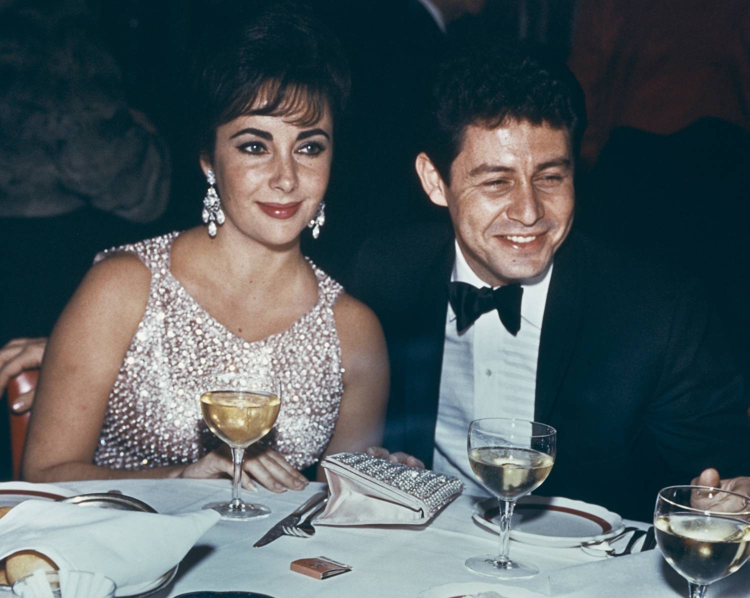 Elizabeth Taylor and Eddie Fisher dining at an event, circa 1959. Taylor wears a silver beaded dress.