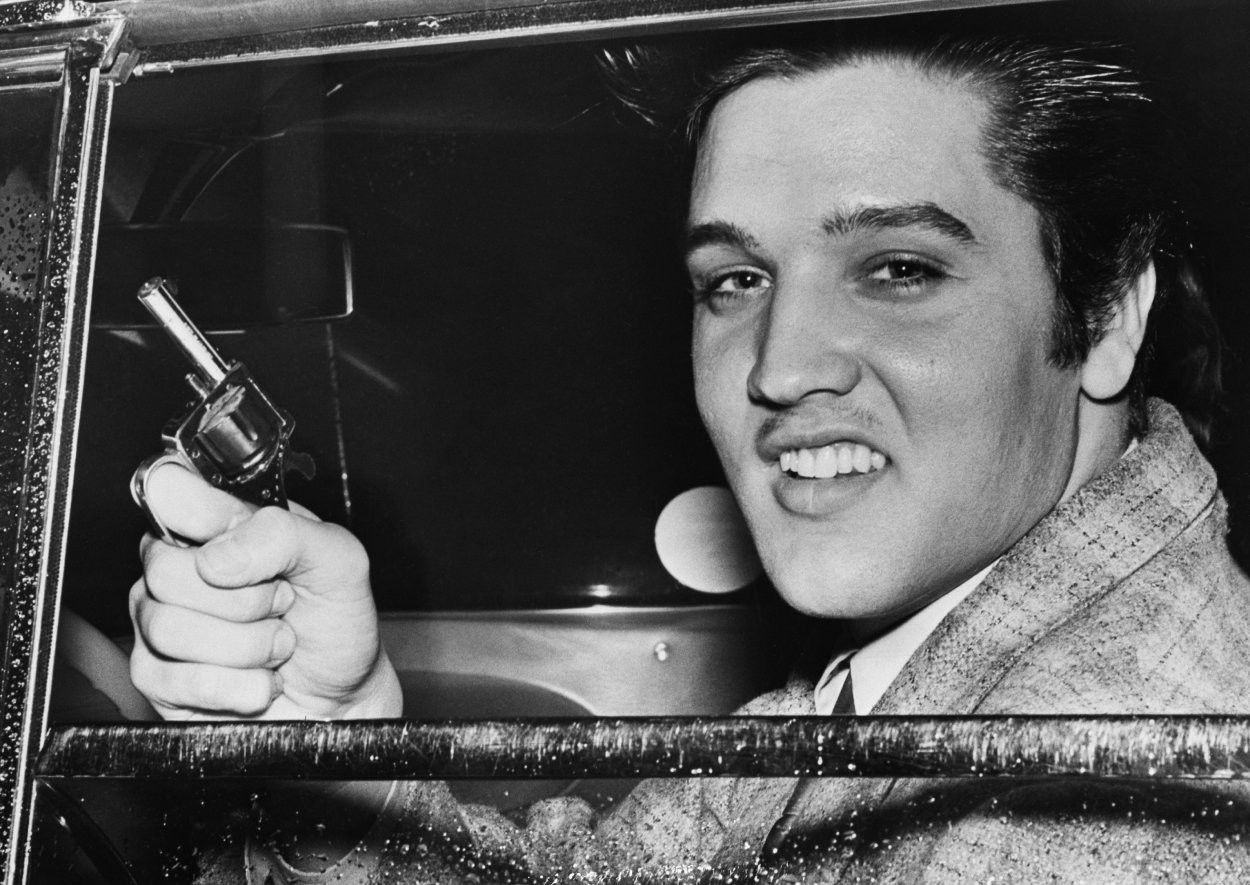 Elvis Presley smiles from a car holding a toy gun