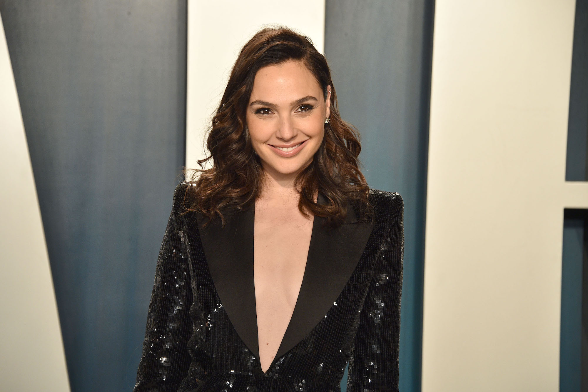 Gal Gadot smiling in front of a blue and white background