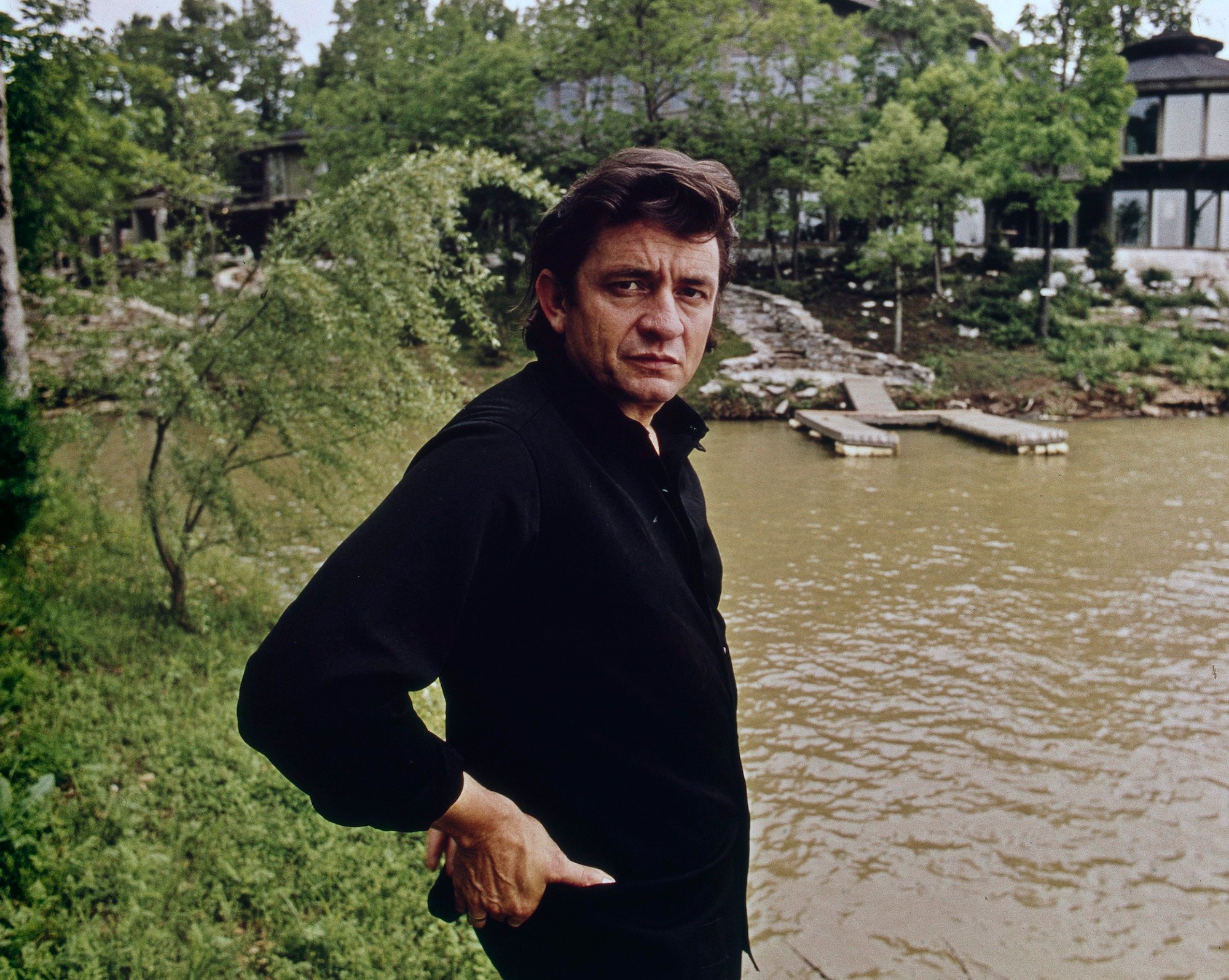 Johnny Cash standing with hands on hips, turned to the camera, in front of a watefront