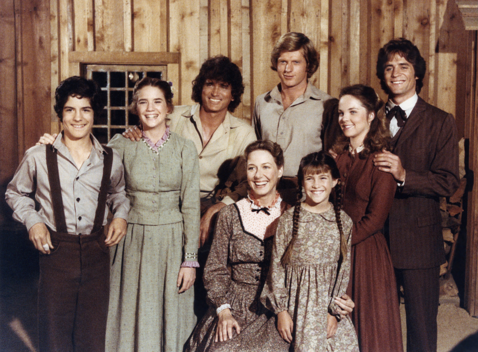 (Top L-R) Matthew Laborteaux as Albert Quinn Ingalls, Melissa Gilbert as Laura Elizabeth Ingalls Wilder, Michael Landon as Charles Philip Ingalls, Dean Butler as Almanzo James Wilder, Melissa Sue Anderson as Mary Ingalls Kendall, Linwood Boomer as Adam Kendall (Bottom L-R) Karen Grassle as Caroline Quiner Holbrook Ingalls, Lindsay/Sidney Greenbush as Carrie Ingalls smiling in front of a wood paneled background