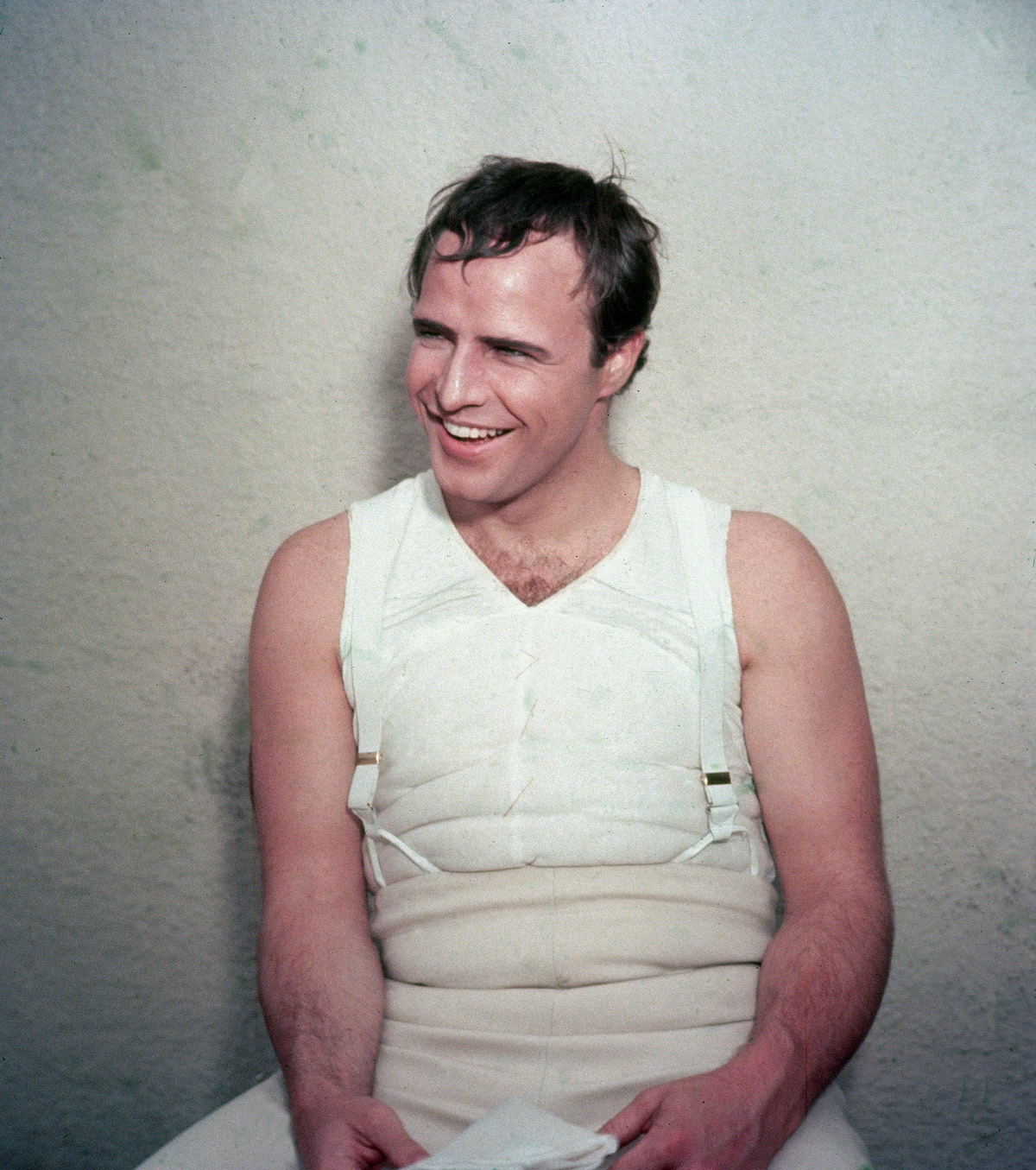 American actor Marlon Brando (1924 - 2004) laughs while wearing body padding for his role as French emperor Napoleon Bonaparte in the film, 'Desiree,' directed by Henry Koster, 1954 | Hulton Archive/Getty Images